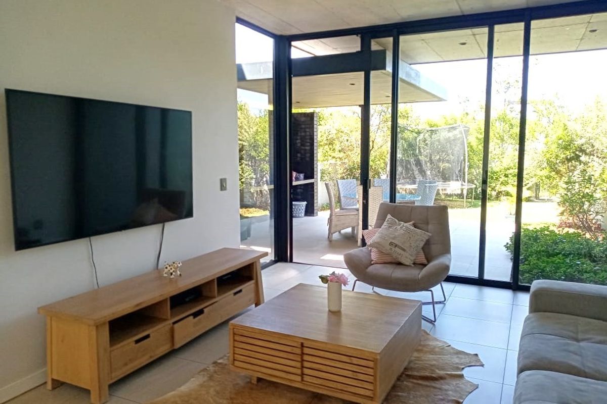 Modern living room featuring an exposed concrete ceiling, large sliding glass doors providing seamless indoor-outdoor flow, and neutral tiled flooring.