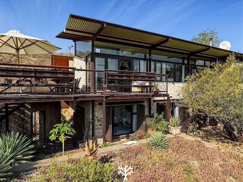 Rear view of a modern multi-level home featuring a raised timber deck, steel structural elements, and large sliding glass doors overlooking a landscaped garden.
