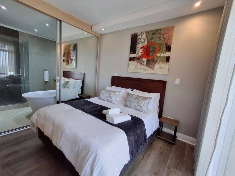 Modern bedroom featuring laminate flooring, recessed lighting, and mirrored sliding wardrobes with an integrated en-suite bathroom containing a freestanding bathtub.