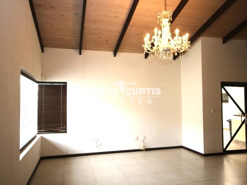 Spacious living area featuring high ceilings with exposed timber beams, tiled flooring, and a decorative chandelier, offering a bright and open atmosphere.