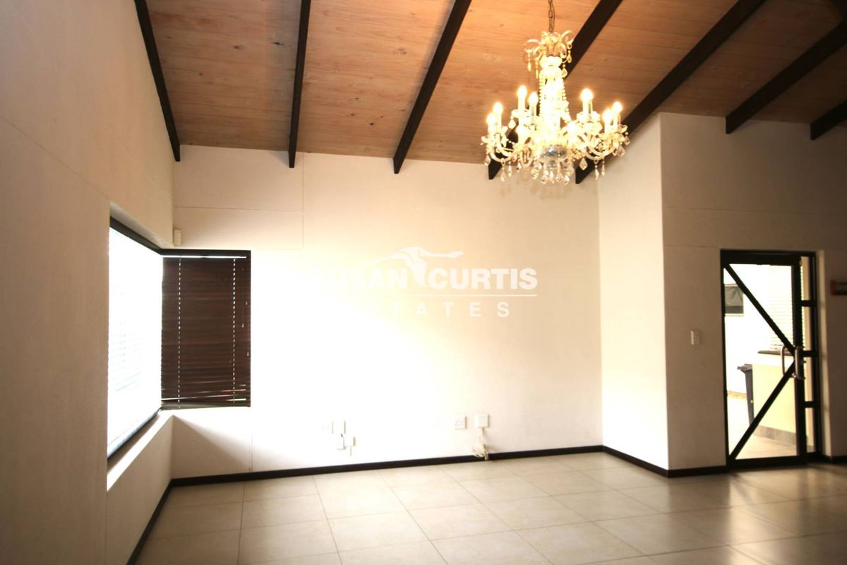 Spacious living area featuring high ceilings with exposed timber beams, tiled flooring, and a decorative chandelier, offering a bright and open atmosphere.