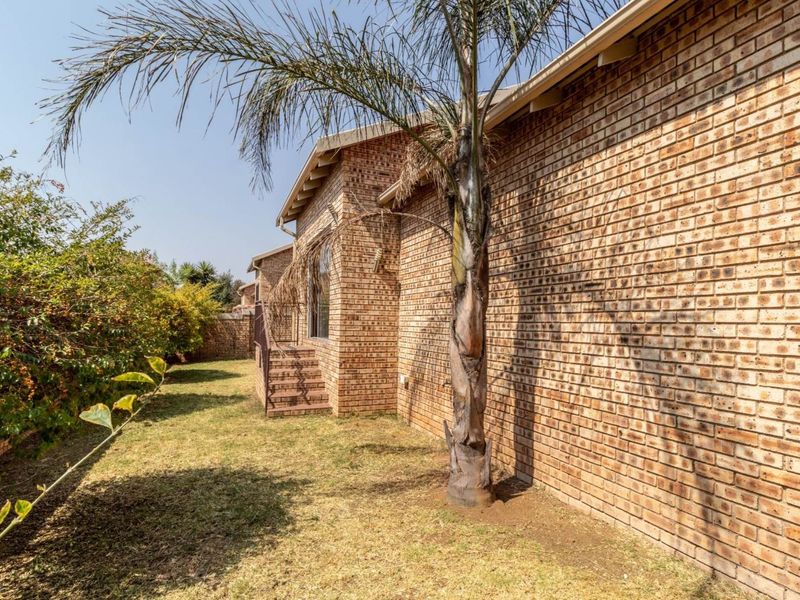 A view of the rear exterior of the townhouse, featuring a face brick facade, garden area, and access to the living space via a sliding door.