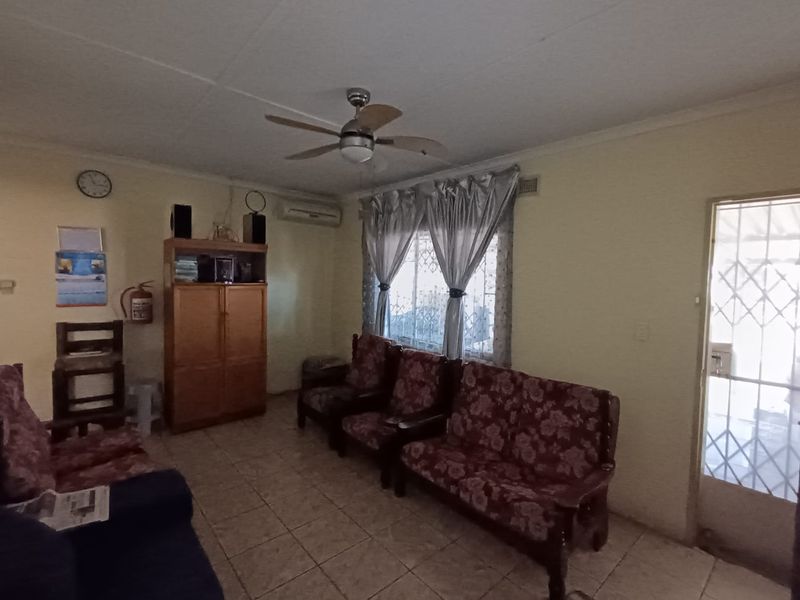 A functional living room featuring tiled flooring, a ceiling fan, and a wall-mounted air conditioning unit, with security features on windows and doors.