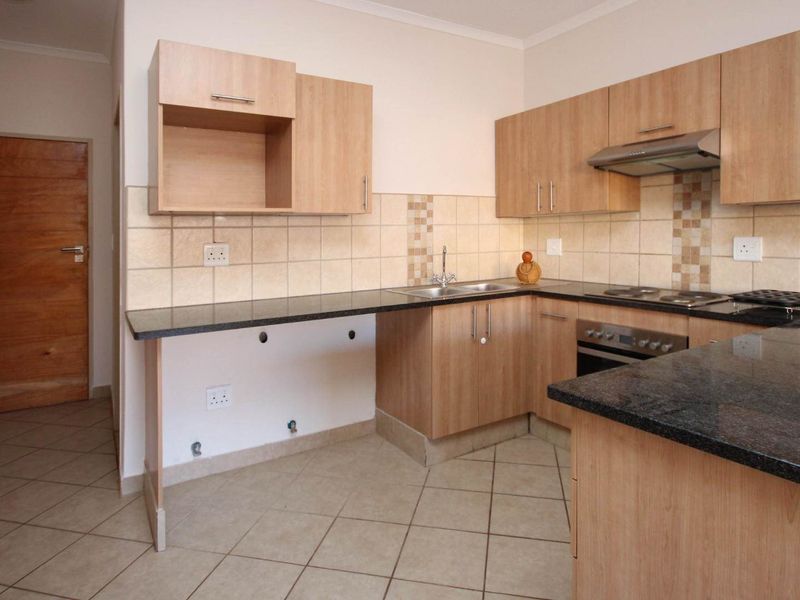 A functional kitchen featuring light wood cabinetry, dark granite countertops, built-in oven, hob, and extractor fan with tiled flooring and backsplash.