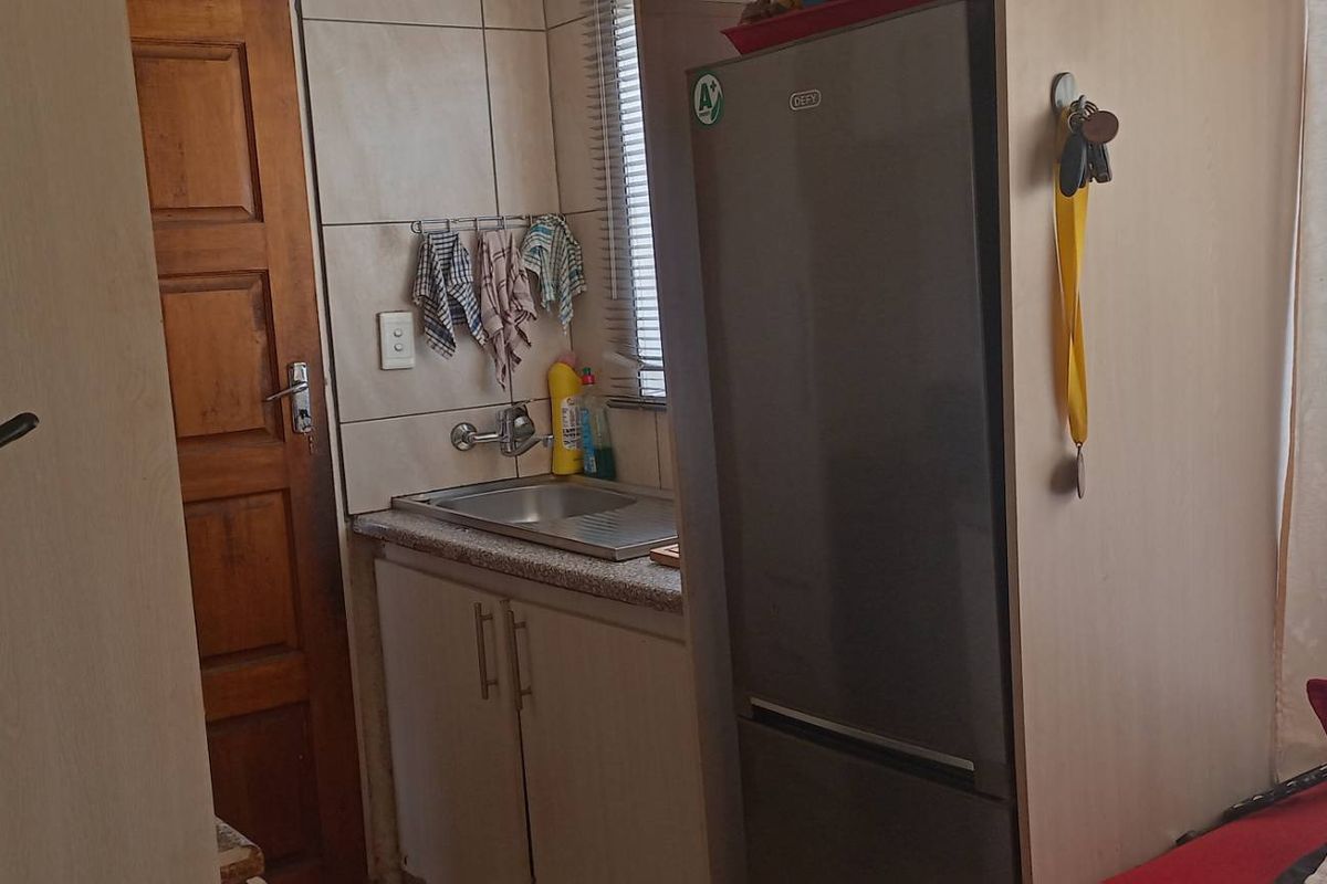 A compact kitchen area featuring a stainless steel sink, built-in cabinetry, and tiled splashback, providing essential utility space.