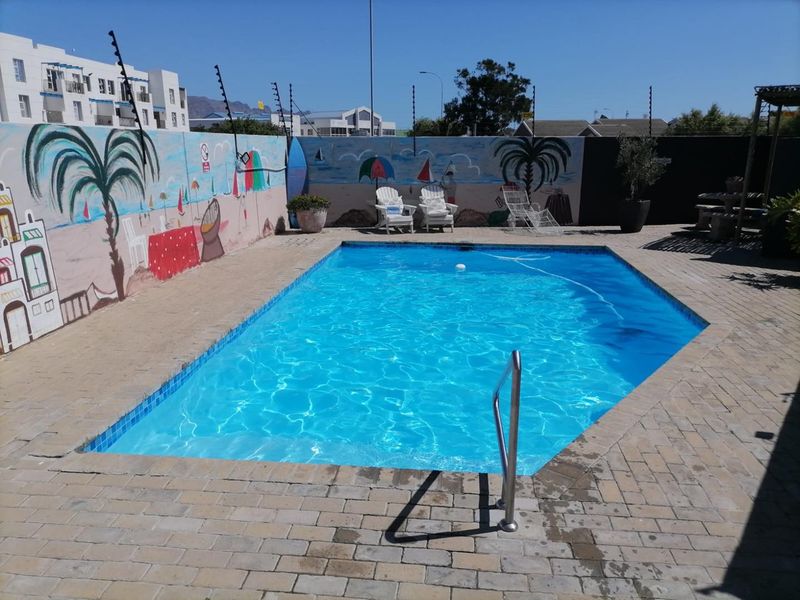 A private outdoor swimming pool area featuring a paved deck, boundary wall with mural, and integrated electric fencing for security.