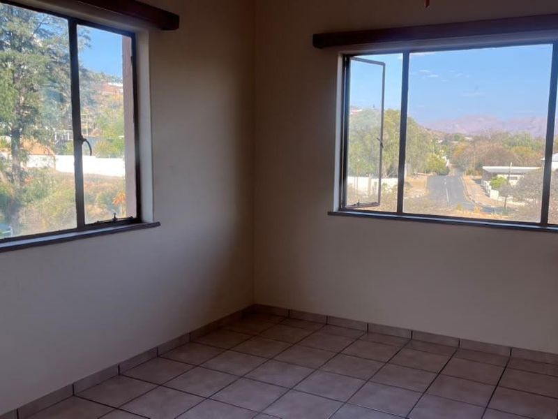 An empty bedroom featuring tiled flooring and large windows that provide ample natural light and scenic views of the surrounding neighborhood.