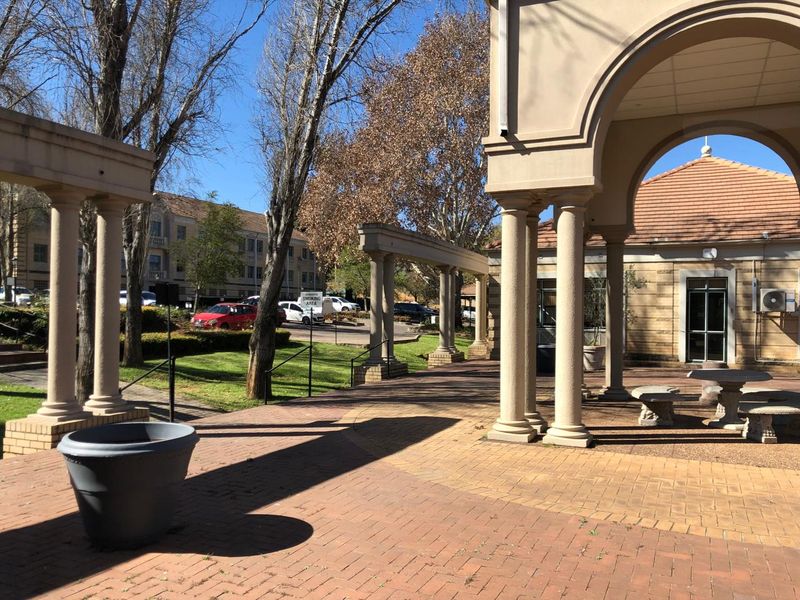 A spacious outdoor patio area featuring classical columns, an arched portico, and brick paving, providing a covered transition space for the office building.