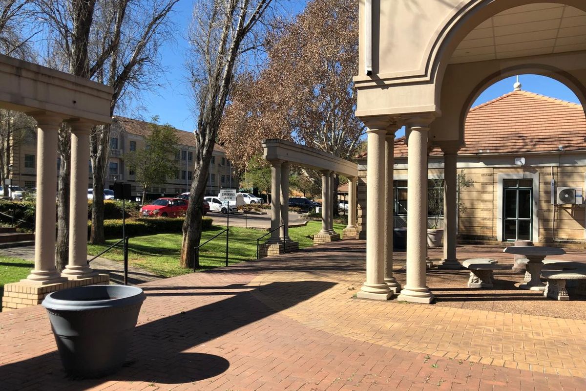 A spacious outdoor patio area featuring classical columns, an arched portico, and brick paving, providing a covered transition space for the office building.
