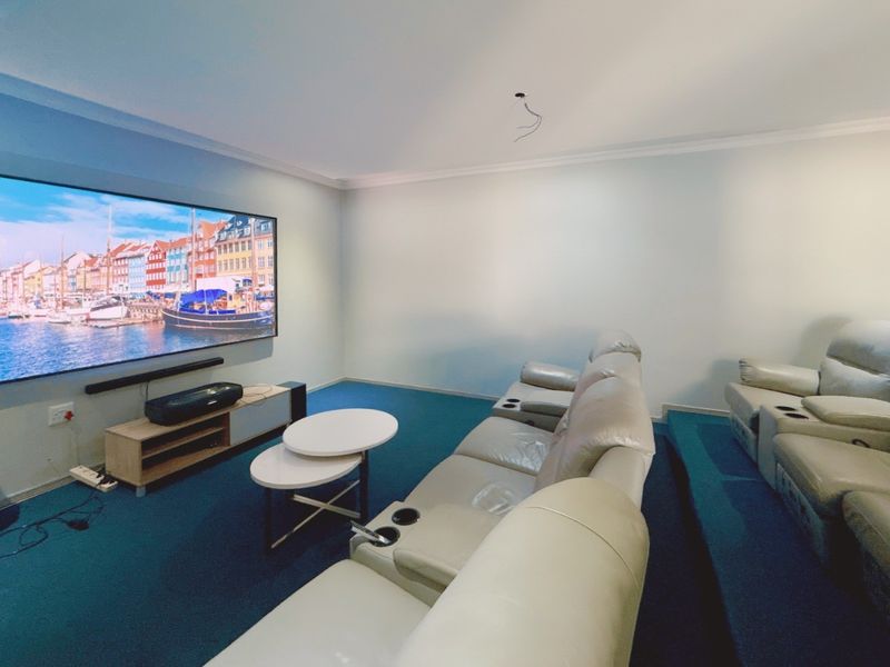 Dedicated cinema room featuring tiered flooring, blue carpeting, and a large wall-mounted screen setup.