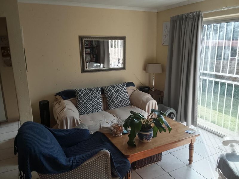 A comfortable living room featuring tiled flooring and a sliding glass door with security gate, providing direct access to the outdoor area.