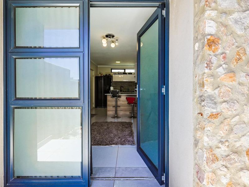 View through an open glass door into a modern kitchen area, featuring stone cladding on the exterior wall and tiled flooring.