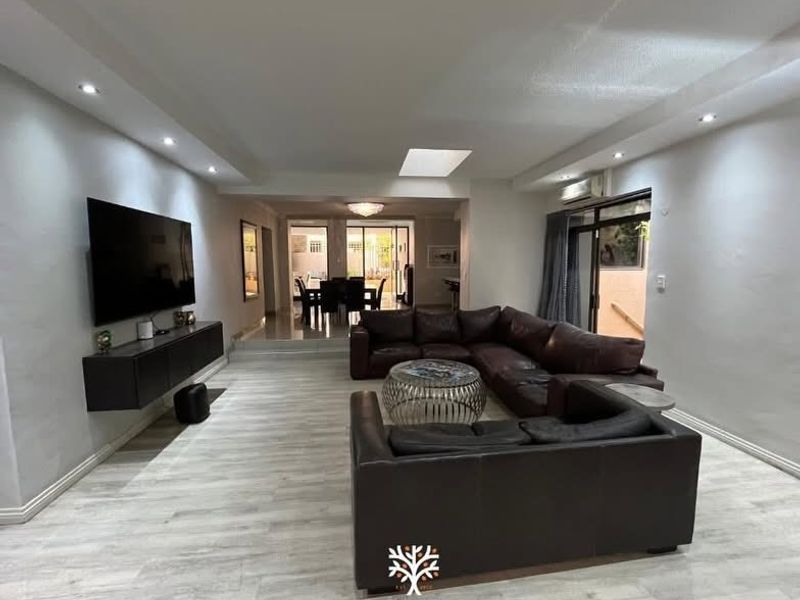 Spacious open-plan living area featuring modern tiled flooring, recessed lighting, a skylight, and wall-mounted cabinetry, flowing into a dining space.