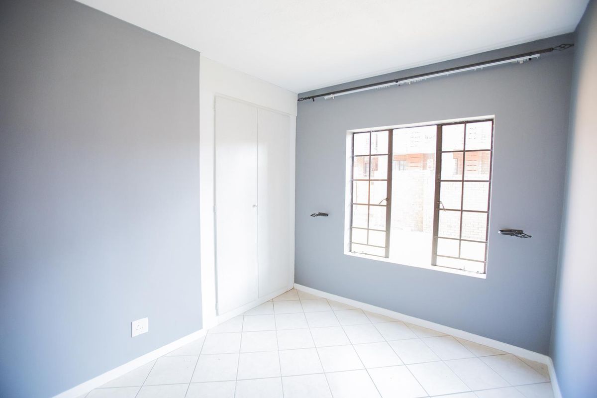 A bright, empty bedroom featuring neutral grey walls, tiled flooring, and a built-in cupboard with a window overlooking the exterior.