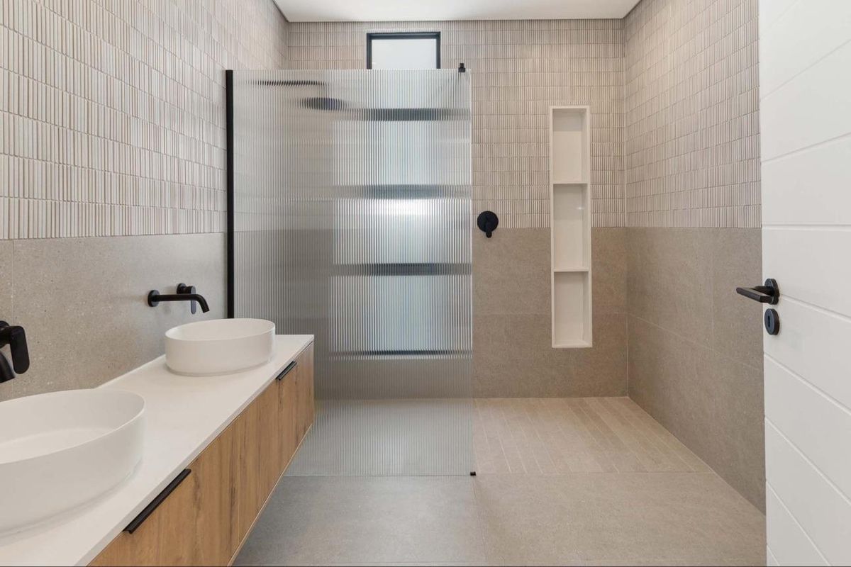 Modern bathroom featuring a double vanity with vessel sinks, wall-mounted matte black faucets, and a spacious walk-in shower with a fluted glass screen.