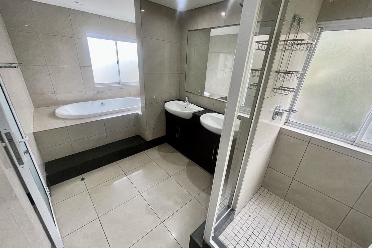 A spacious, modern bathroom featuring a double vanity, a built-in bathtub, and a separate glass-enclosed shower with neutral floor-to-ceiling tiling.