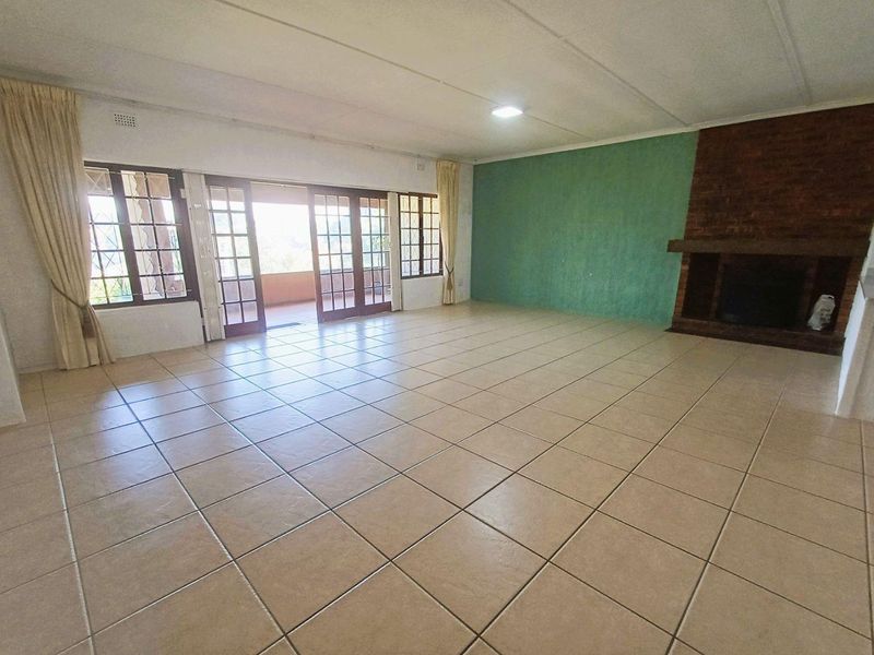 Spacious living room featuring tiled flooring, a prominent brick fireplace, and large french doors opening to an outdoor patio area.