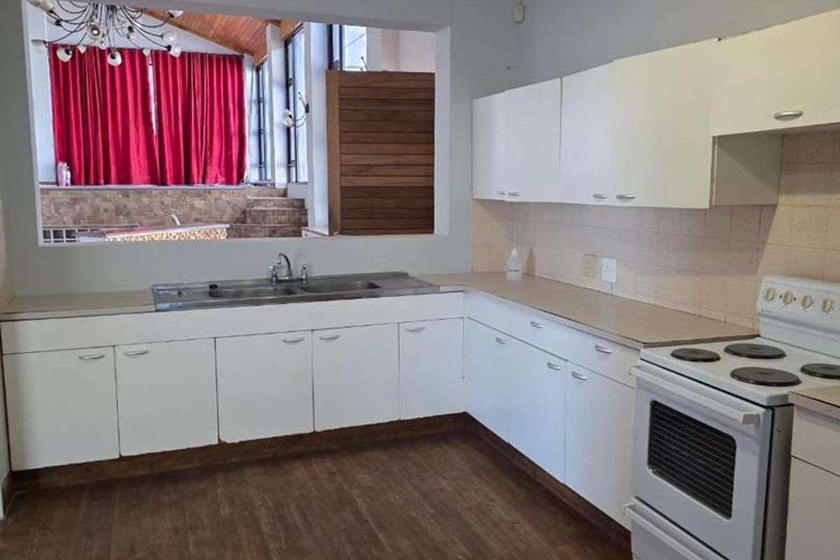 A functional kitchen featuring white cabinetry, a stainless steel sink, and a pass-through window overlooking an adjacent living area.