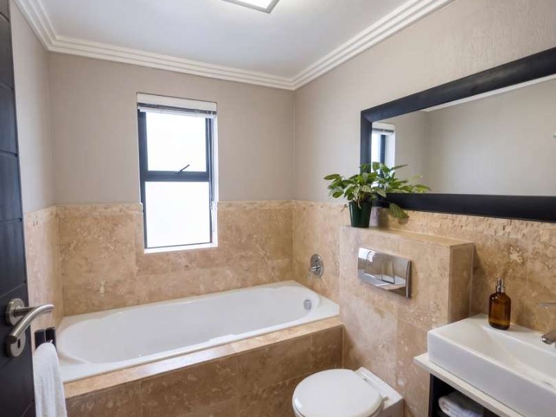A well-maintained bathroom featuring stone wall tiling, a built-in bathtub, a wall-mounted toilet, and a modern vanity cabinet with an integrated sink.