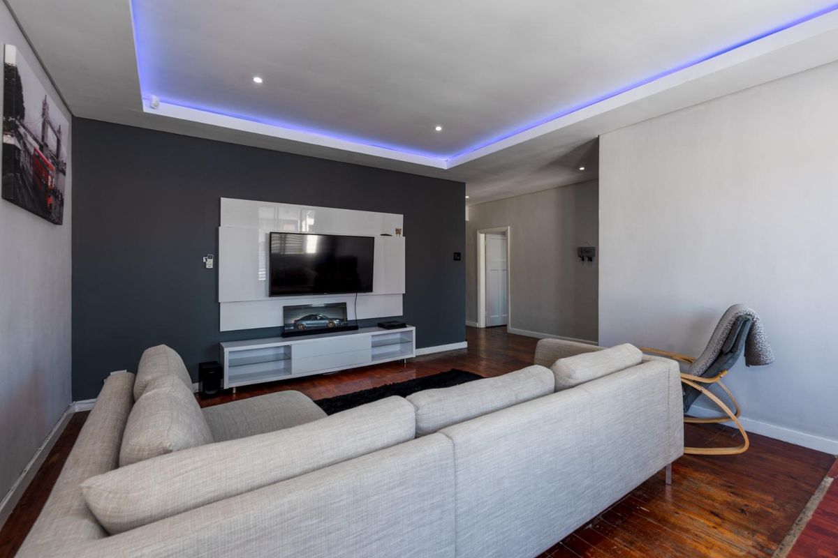 Modern living room featuring hardwood flooring, a built-in media wall unit, and sophisticated recessed ceiling lighting with integrated LED accents.