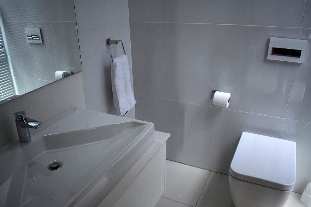A modern bathroom featuring a wall-mounted toilet with a concealed cistern, a sleek vanity basin, and large-format wall tiles.