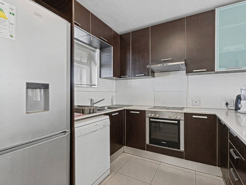 A functional kitchen featuring dark wood cabinetry, built-in oven, electric hob, extractor fan, and tiled flooring with ample counter space.