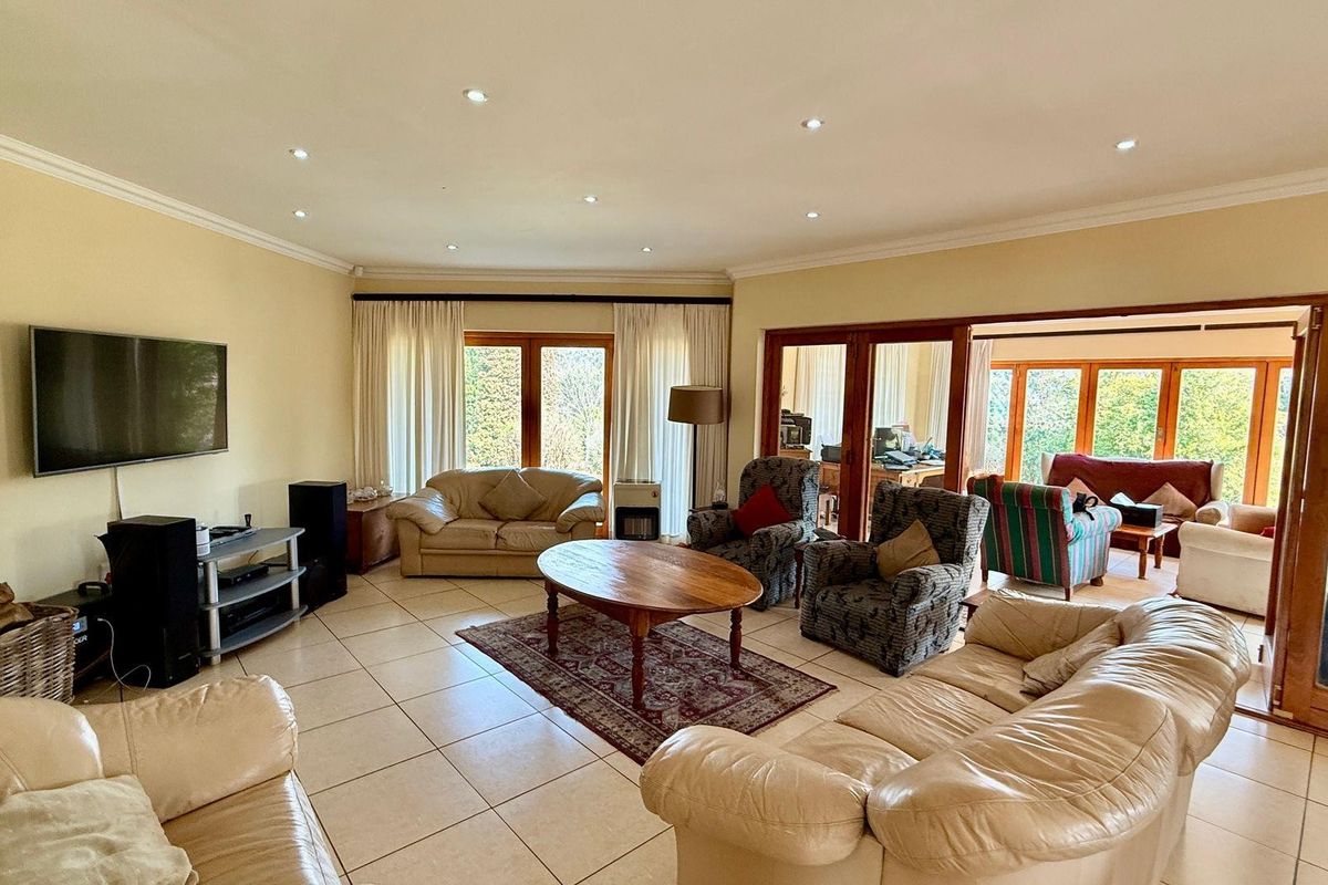 Spacious living room featuring tiled flooring, recessed downlighting, and large glass sliding doors providing access to an adjoining sunroom and garden views.