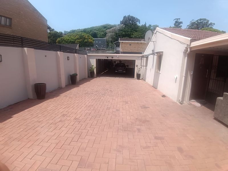 A paved driveway leading to a covered carport area, featuring perimeter boundary walls and a clean, well-maintained exterior facade.