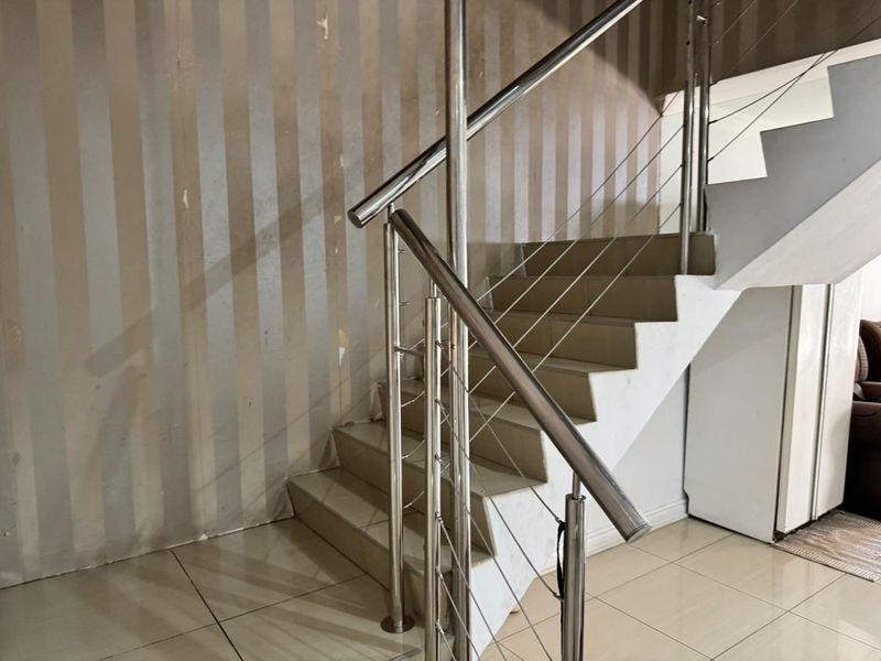 A staircase area featuring tiled steps and a modern stainless steel balustrade, currently showing signs of wear on the wall finishes.