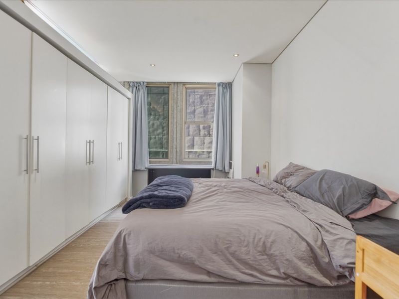 A well-maintained bedroom featuring extensive built-in wardrobes, recessed downlighting, and modern timber flooring, offering a clean and functional living space.
