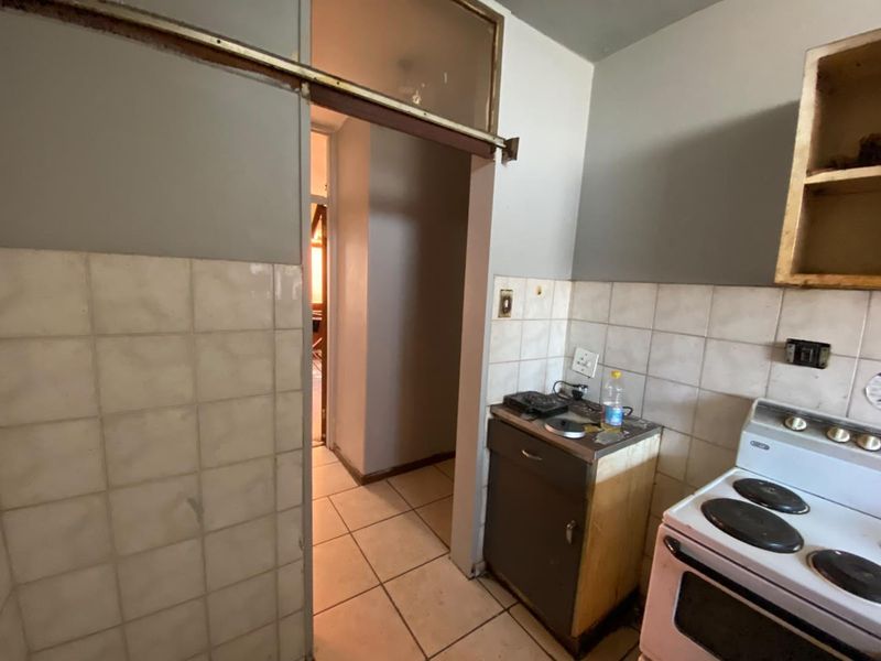 A compact kitchen area featuring tiled splashbacks, ceramic flooring, and a built-in stove, currently requiring significant renovation and cosmetic updates.
