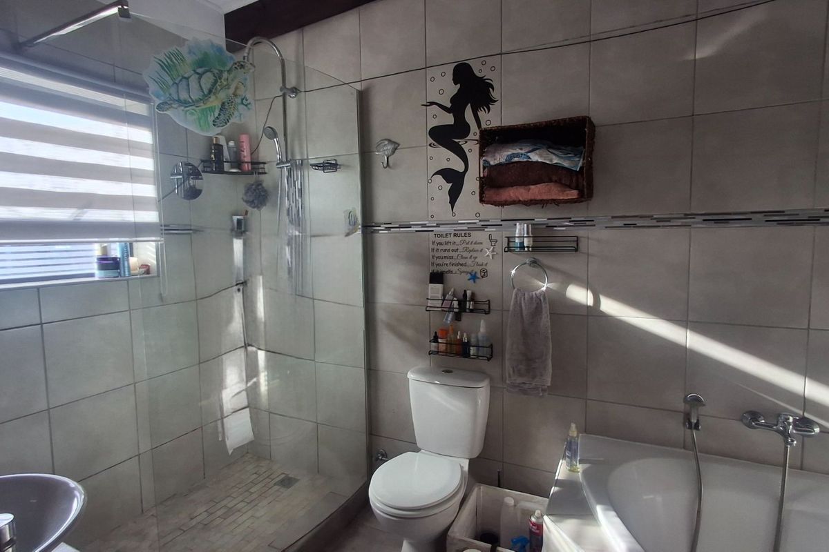 A functional bathroom featuring a glass-enclosed shower, a bathtub with a handheld mixer, and neutral wall tiling.