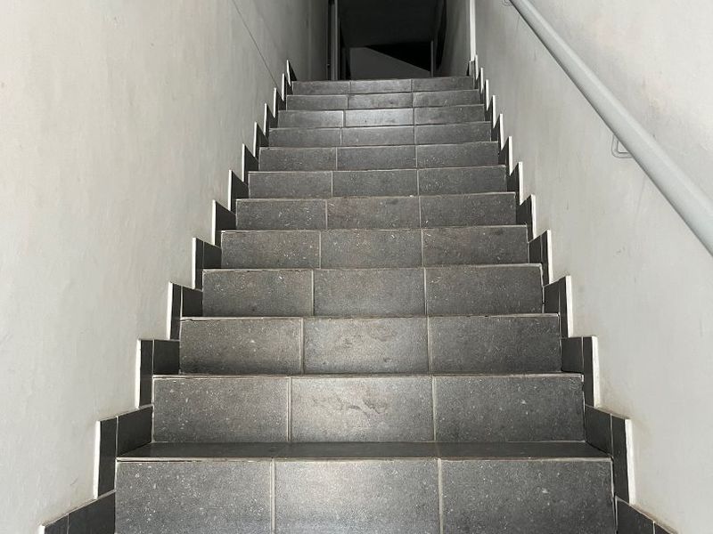 A functional interior staircase featuring dark grey tiled steps and a mounted handrail, providing access between levels in an industrial property.