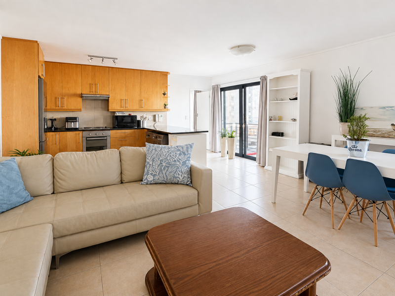 Open-plan living and dining area featuring a functional kitchen with wood-finish cabinetry, tiled floors, and direct access to a balcony through sliding glass doors.