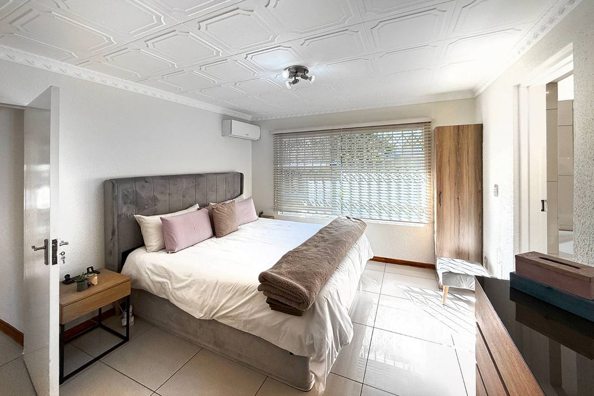 A well-maintained bedroom featuring tiled flooring, a decorative coffered ceiling, and a wall-mounted air conditioning unit.