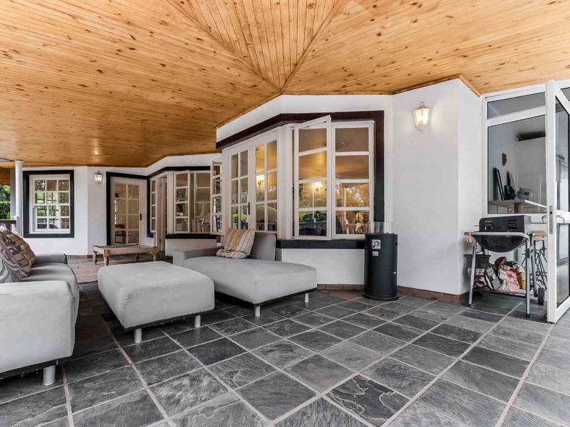 A spacious covered patio featuring a warm timber-clad ceiling, durable slate tile flooring, and multiple windows providing natural light and access to the home.