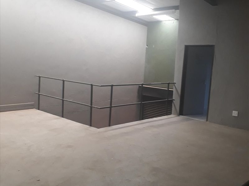 An open-plan industrial mezzanine level featuring concrete flooring, exposed steel structural beams, skylights, and a metal safety railing.