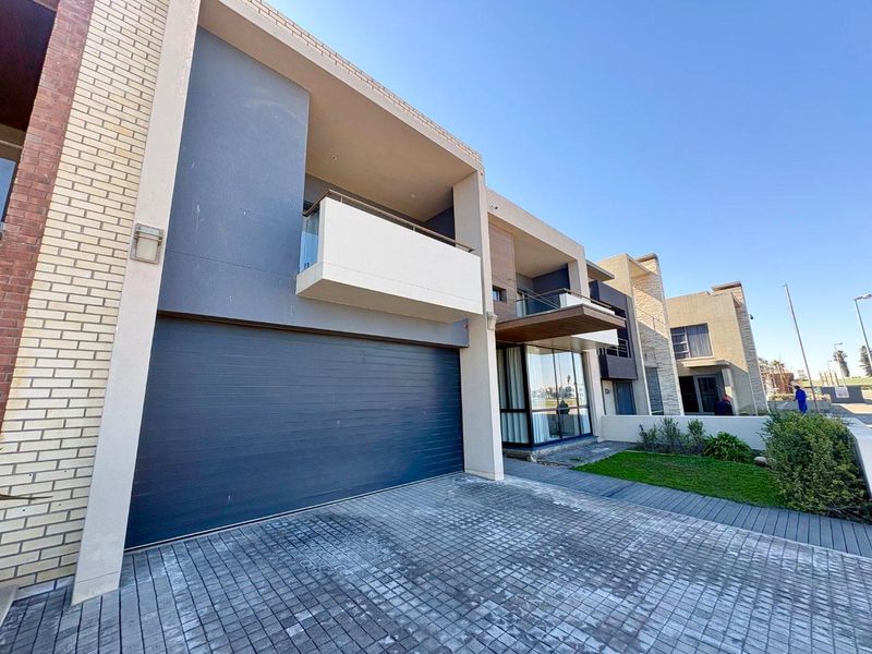 Modern multi-story residential facade featuring a paved driveway, integrated garage, and upper-level balcony with glass balustrade.