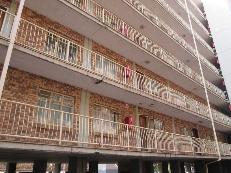 Exterior view of a multi-story apartment building featuring brick facade, concrete walkways, and metal balcony railings with visible signs of wear.