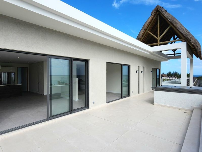 Spacious penthouse balcony featuring large sliding glass doors, modern tiled flooring, and a unique thatched roof architectural detail with panoramic views.