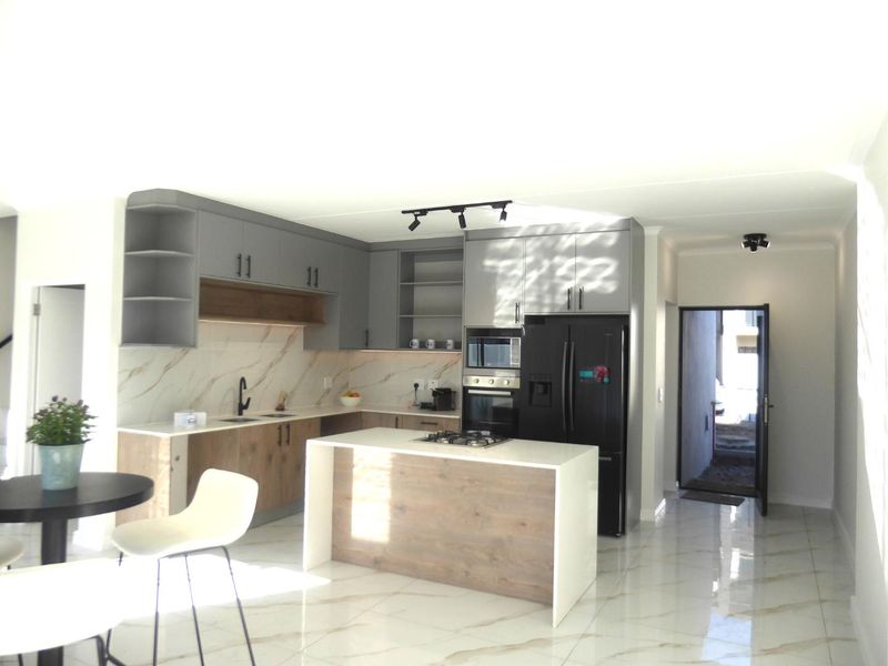 Modern kitchen featuring two-tone cabinetry, stone countertops, a central island with a gas cooktop, and high-end built-in appliances with polished tiled flooring.