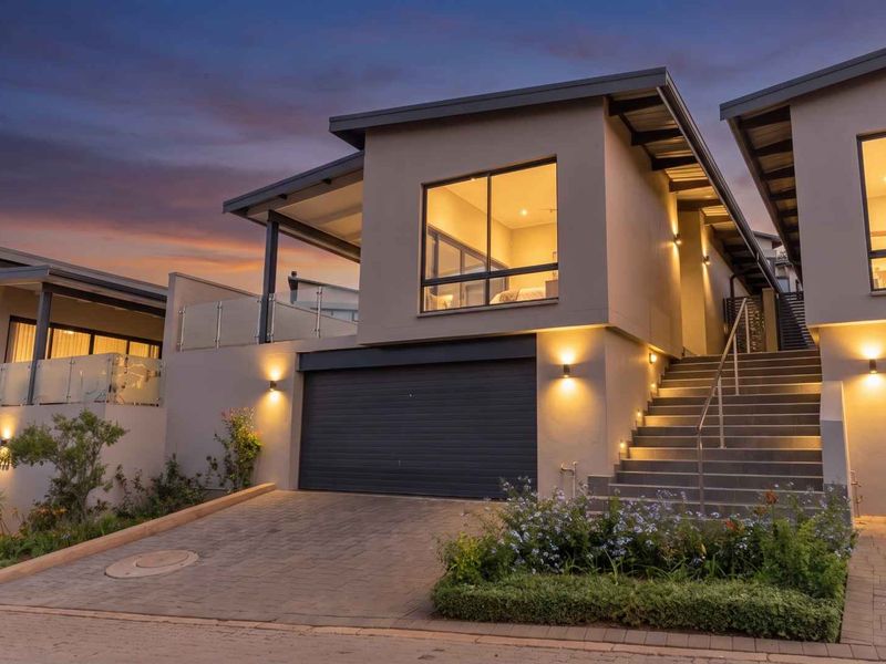 Modern cluster home exterior featuring a double garage, paved driveway, and an illuminated staircase leading to an elevated balcony area.