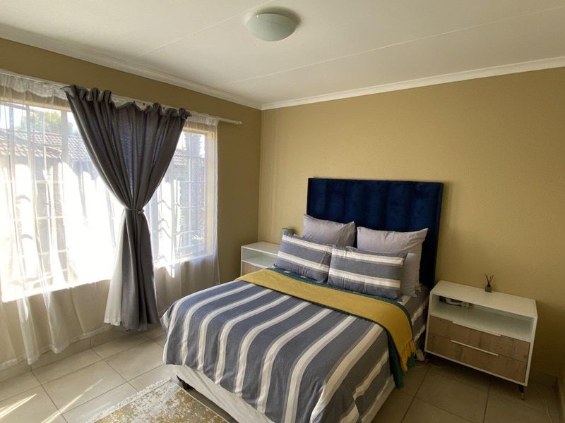 A well-lit bedroom featuring tiled flooring, neutral wall tones, and a window fitted with security bars.