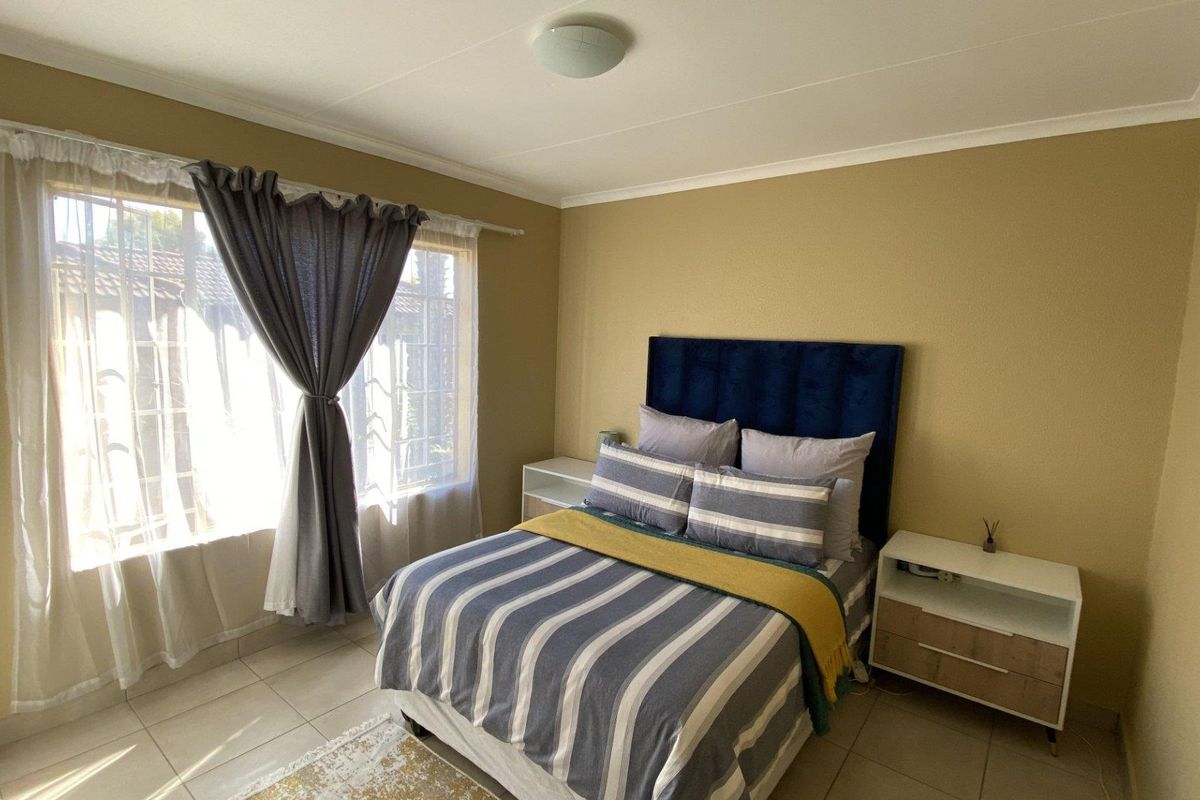 A well-lit bedroom featuring tiled flooring, neutral wall tones, and a window fitted with security bars.