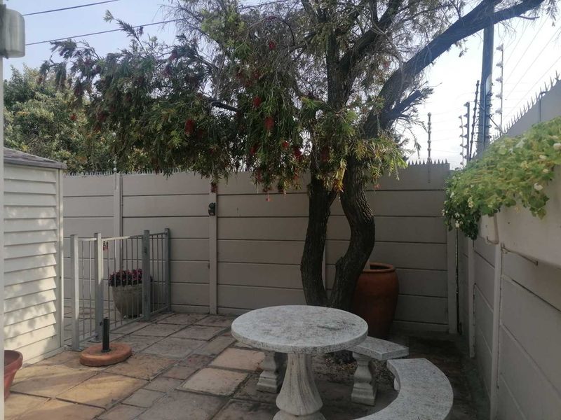 A private rear courtyard featuring paved flooring, secure perimeter walling with electric fencing, and a mature tree providing shade.