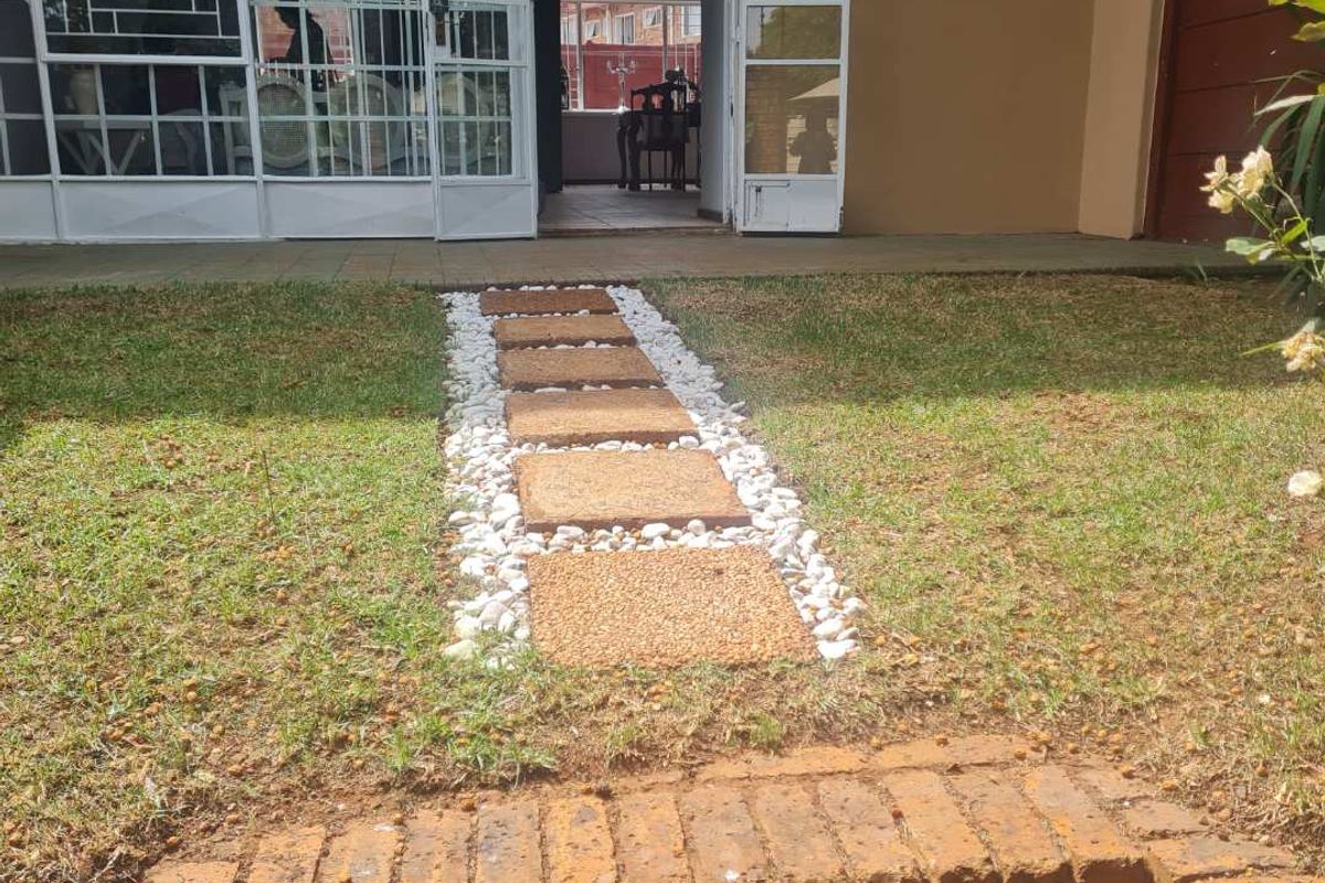 Rear exterior view featuring a brick pathway with pebble borders leading to a glass sliding door and metal security gate.