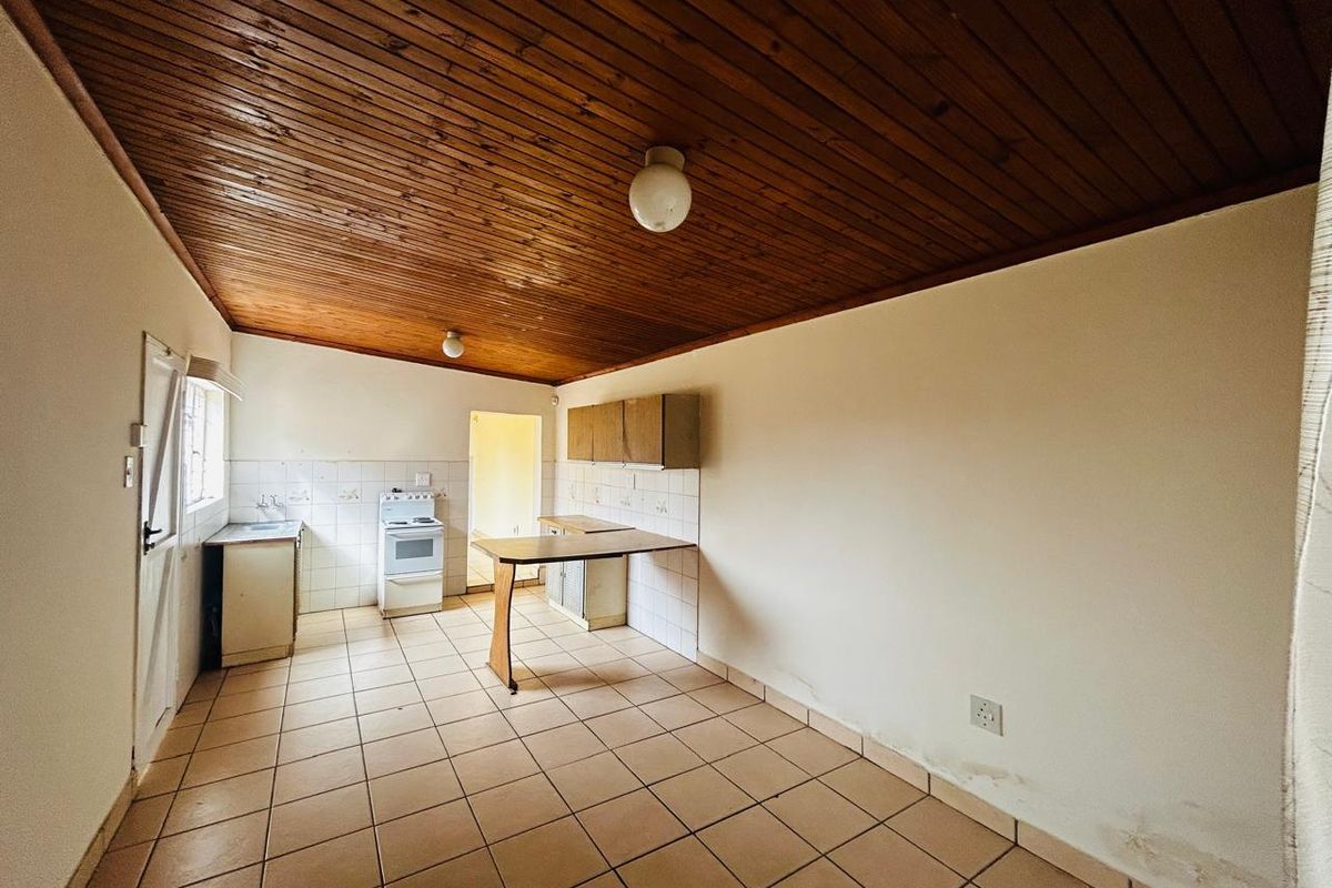 A dated kitchen featuring tiled flooring, a wood-paneled ceiling, basic cabinetry, and a freestanding stove, offering potential for a modern renovation.