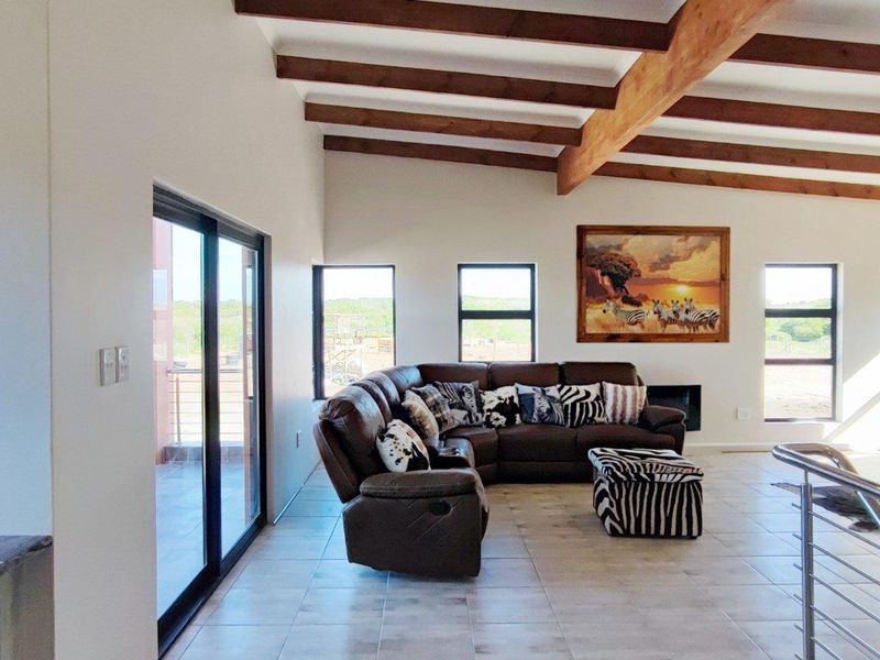 Spacious living area featuring exposed timber ceiling beams, tiled flooring, a built-in fireplace, and large windows providing natural light and scenic views.