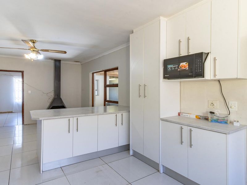 Kitchen area featuring white cabinetry, laminate countertops, built-in microwave, and tiled flooring, adjacent to a living space with a fireplace.
