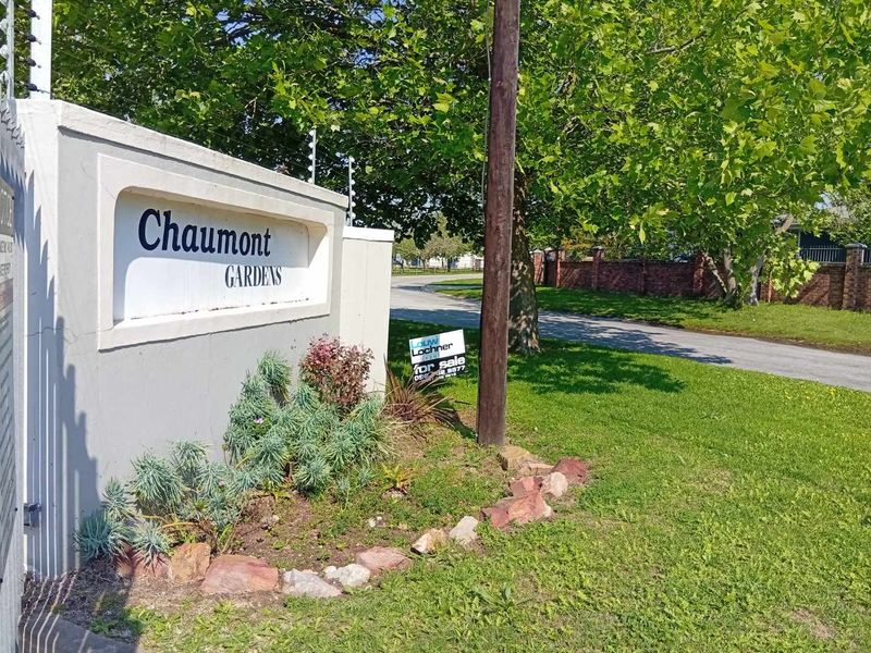 Street view of the Chaumont Gardens complex entrance, featuring a concrete boundary wall with integrated signage and electric security fencing.